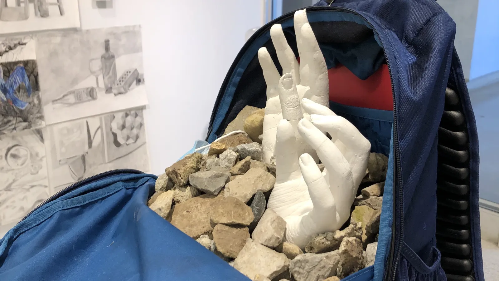 art installation of hands reaching out of rocks contained in back pack