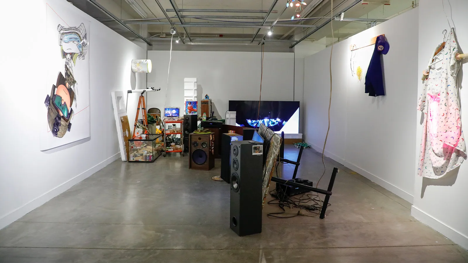 Installation view of mixed media installation with a range of objects and video monitors on floor and walls. 