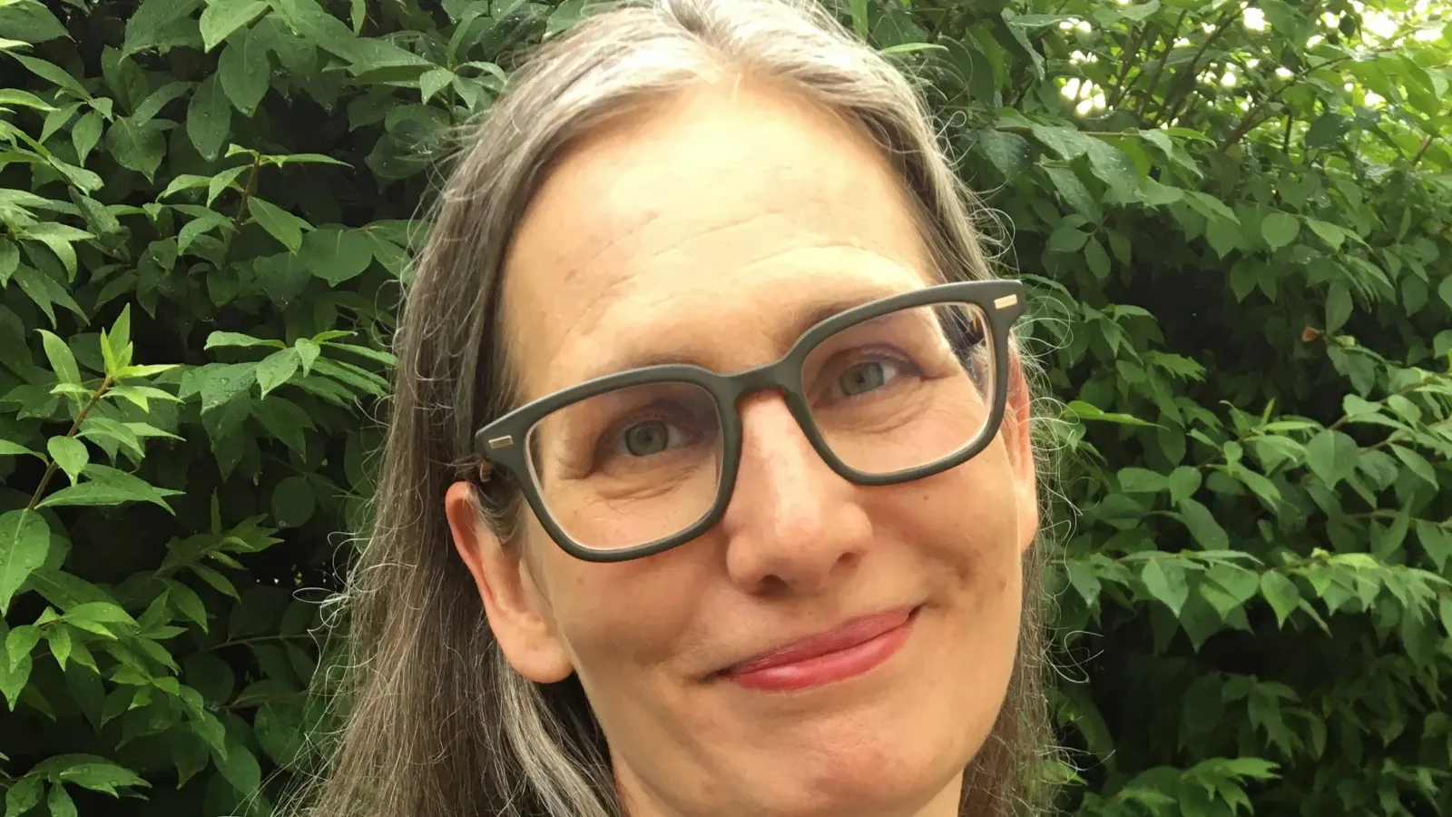 .A headshot of author Laura Larson smiling outdoors against a background of green foliage.