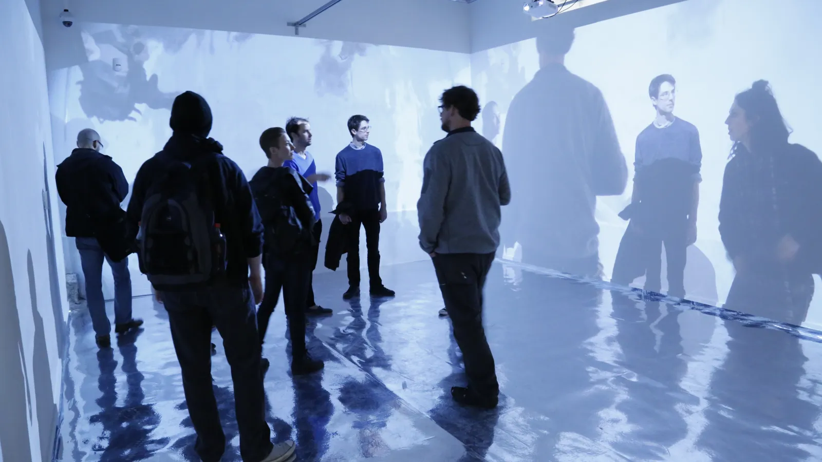 People standing in a gallery-like room with projected silhouettes surrounding them on the walls.