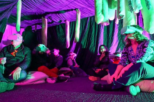 green tubes hanging from the ceiling people sitting underneath wearing virtual reality headsets