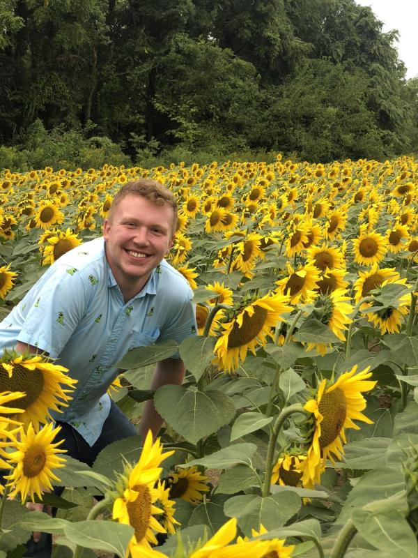 Shawn Knecht in a blue shirt sits in a field of yellow sun flowers