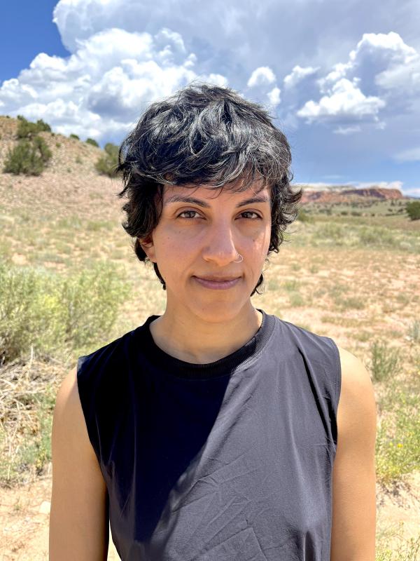 a person with dark hair standing in front of mountains