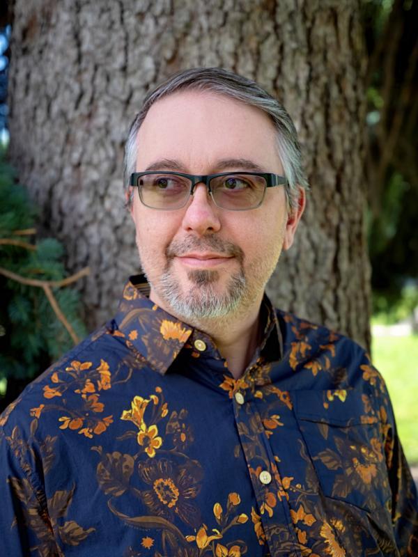 a person with a goatee and  glasses standing inffront of a tree
