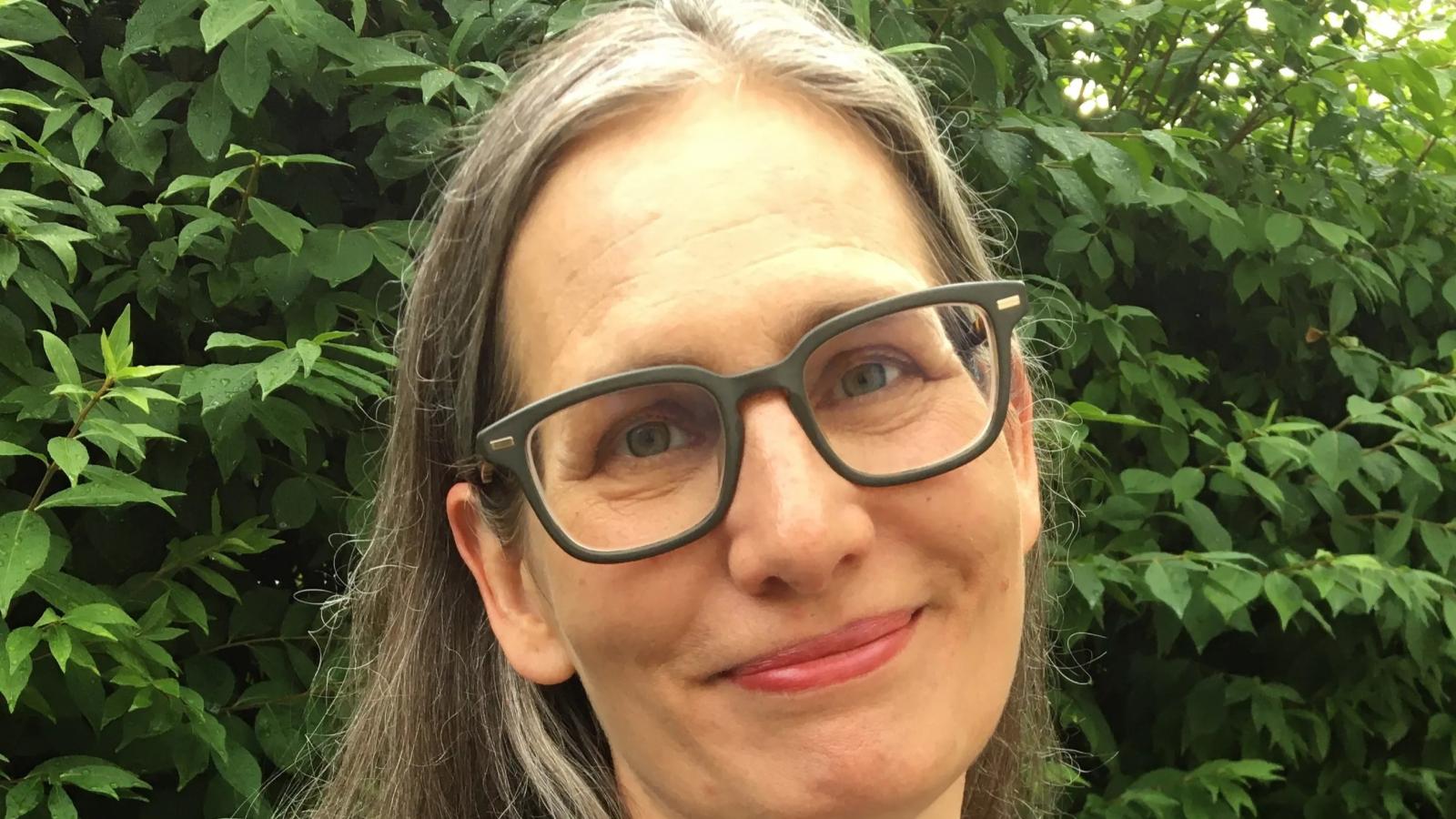 .A headshot of author Laura Larson smiling outdoors against a background of green foliage.